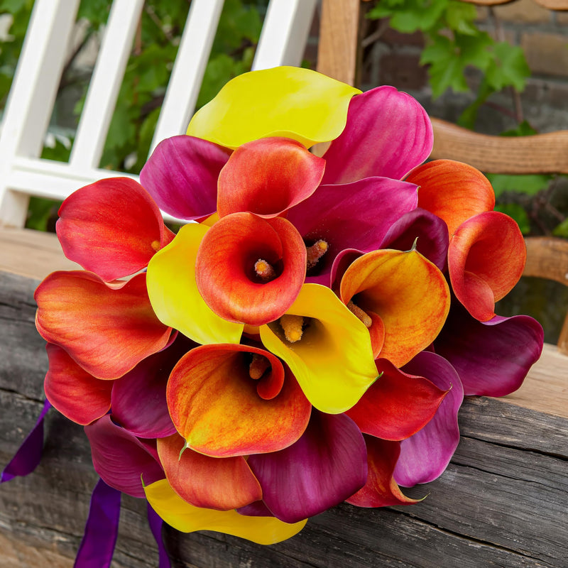 Bouquet of colorful calla lilies on a wooden surface with a blurred natural background